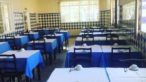 Comedor con varias mesas cubiertas de manteles azules, dispuestas en filas.