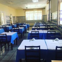 Uma área de refeições com várias mesas cobertas por toalhas azuis, dispostas em fileiras.