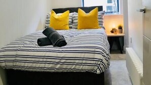 A narrow bedroom with a bed, two yellow pillows, and a black headboard. - ⭐⭐⭐⭐⭐ Beautiful Apartment Near the BEACH +Netflix (Bournemouth)