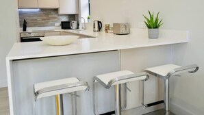 A modern kitchen with a white countertop, stainless steel appliances, and a bar area with stools. - ⭐⭐⭐⭐⭐ Beautiful Apartment Near the BEACH +Netflix (Bournemouth)