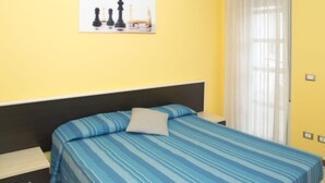 A hotel room with a single bed, a nightstand, a small drawer, and a painting of chess pieces on the wall. - Gattinara Residence - two-room apartment 2 (Savigliano/cuneo)