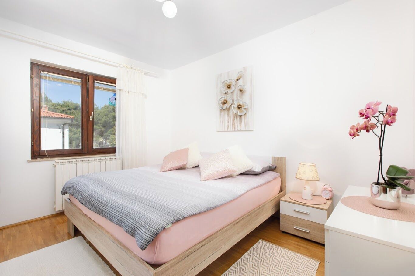 Une chambre à coucher avec un lit, une table de chevet, une lampe, une horloge et une fenêtre avec des rideaux.