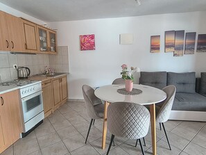 A kitchen with a stove, cabinets, and a dining area with a table and chairs. - Apartments Pepa (Rogoznica)