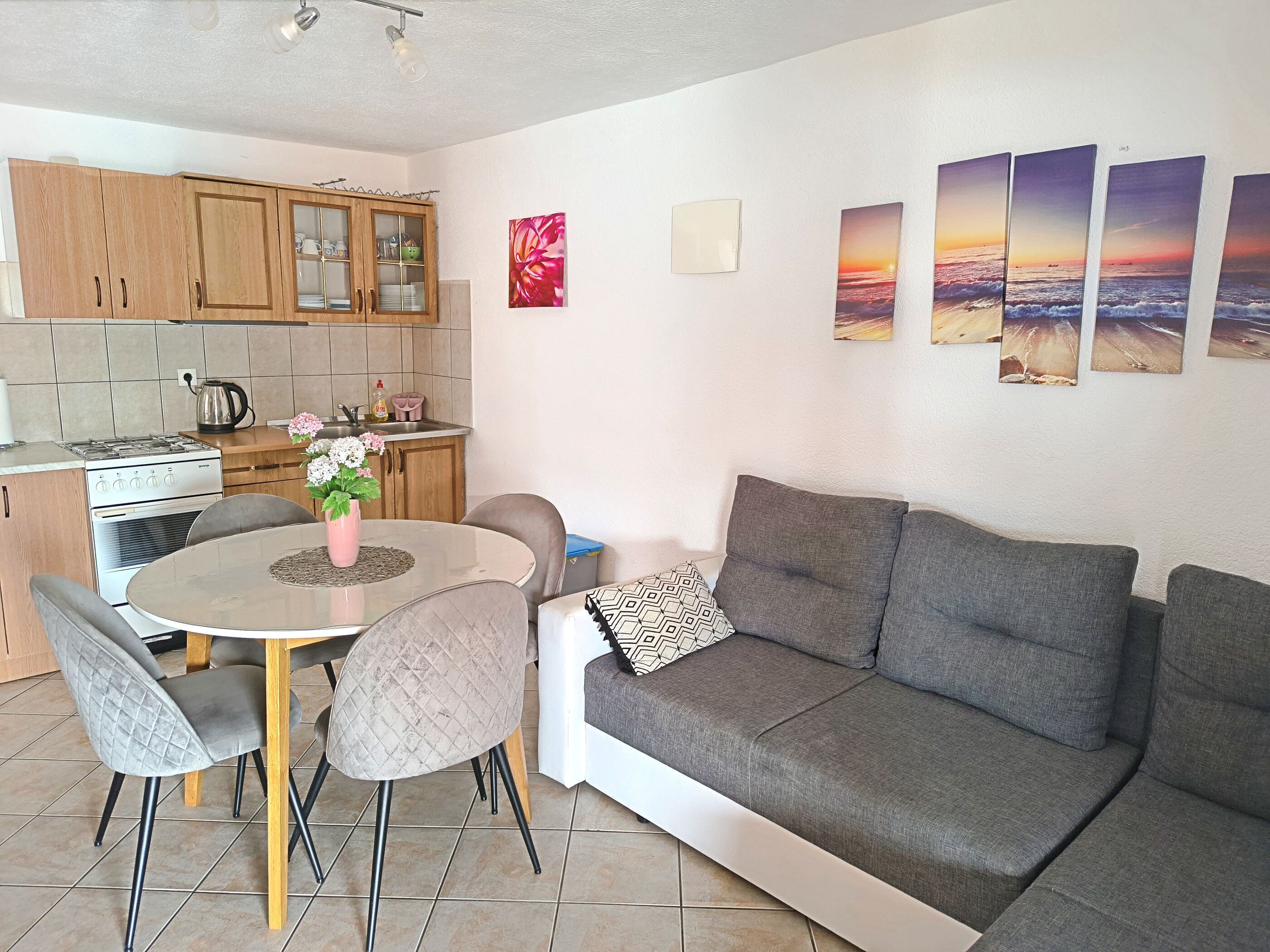 A modern kitchen with wooden cabinets, a dining table with chairs, and a grey sofa.