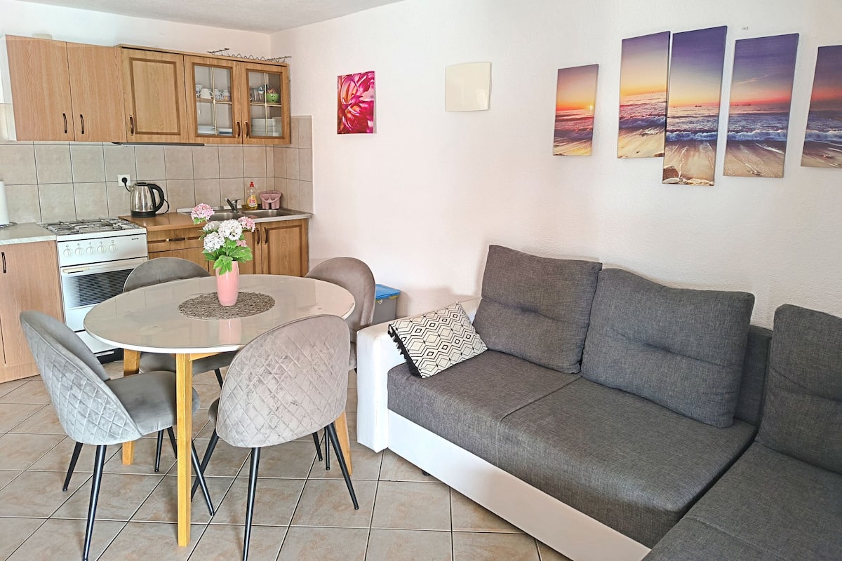 A modern kitchen with wooden cabinets, a dining table with chairs, and a grey sofa.