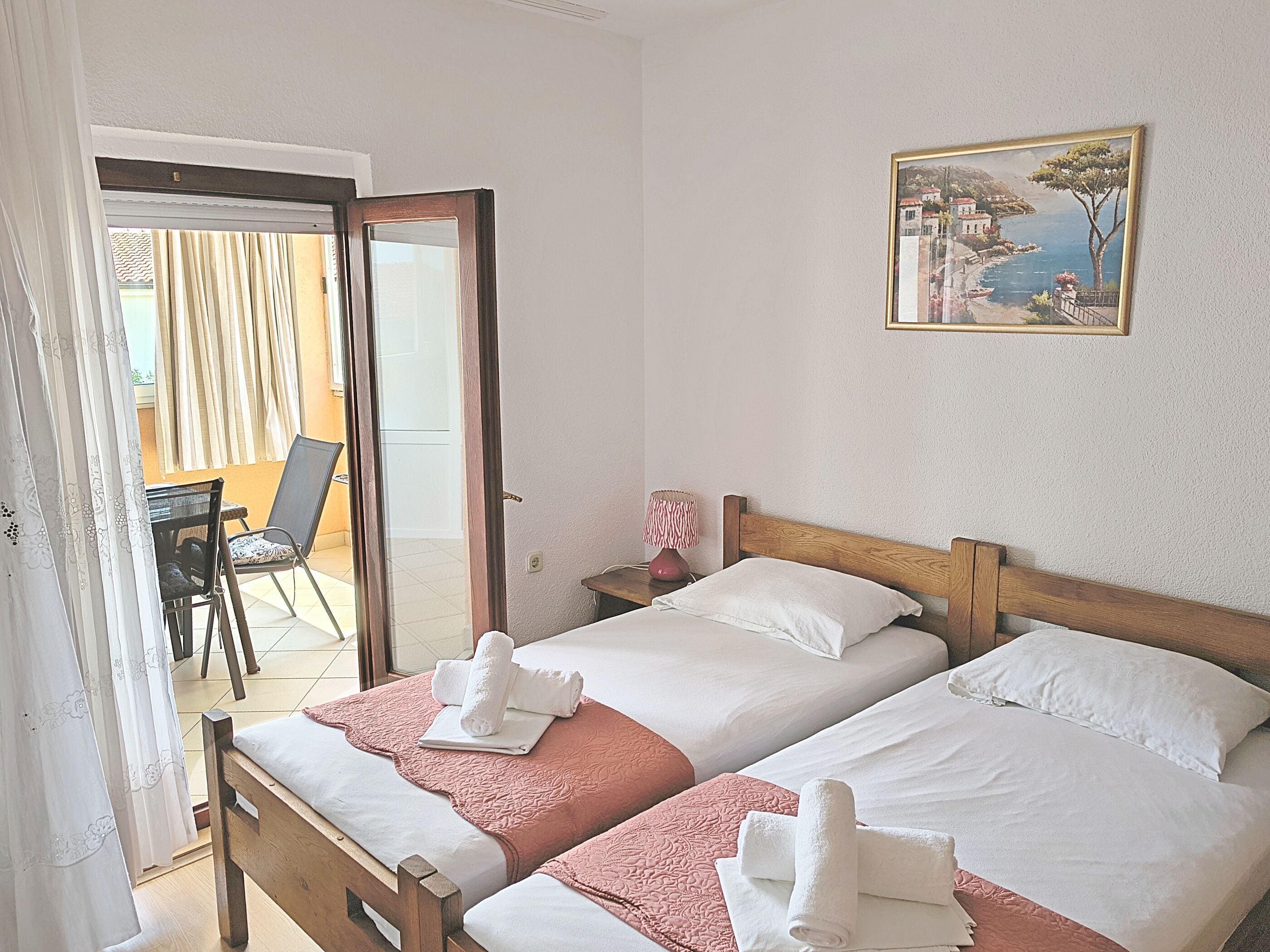 A room with two beds, a painting on the wall, a chair, and a table.