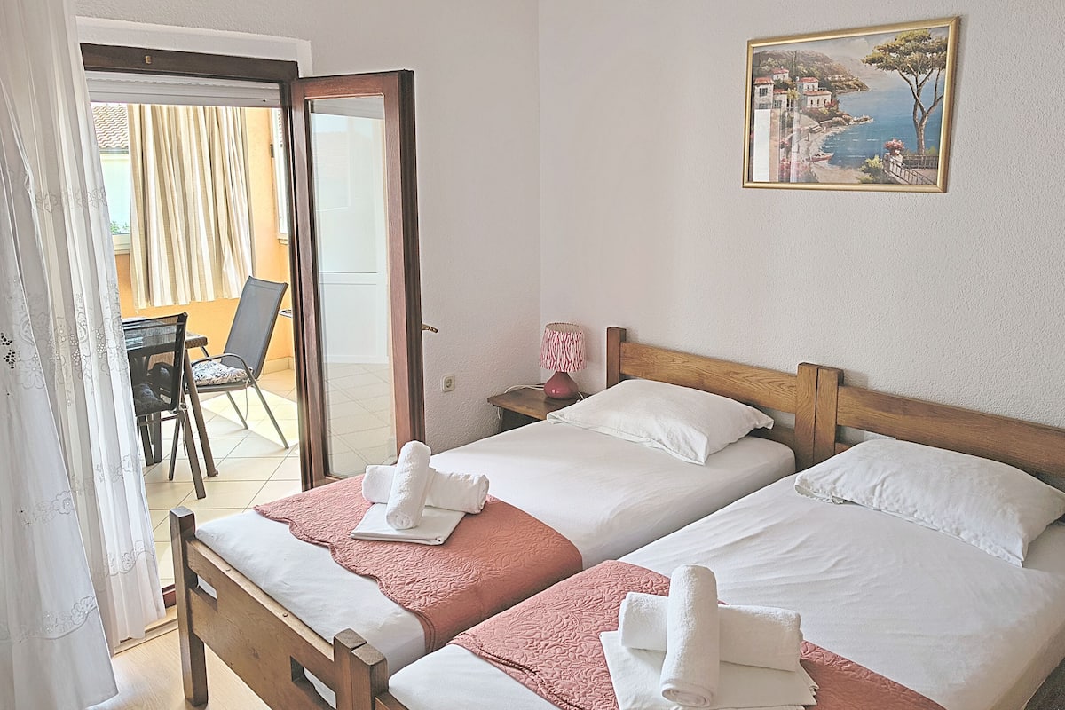 A hotel room with two beds, a painting on the wall, a chair, and a table.