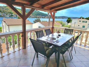 A terrace with a table and chairs, a view of a body of water, and buildings in the background. - Apartments Pepa (Rogoznica)