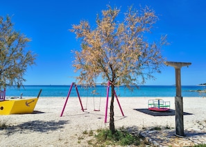 A beach with swings, a yellow boat, and a stone structure. - Apartments Pepa (Rogoznica)