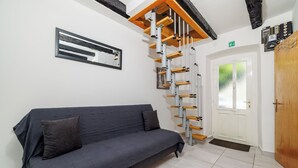 A modern room with a grey sofa, a wooden staircase, a white door, and a small window. - Apartment Lozann (Povile)