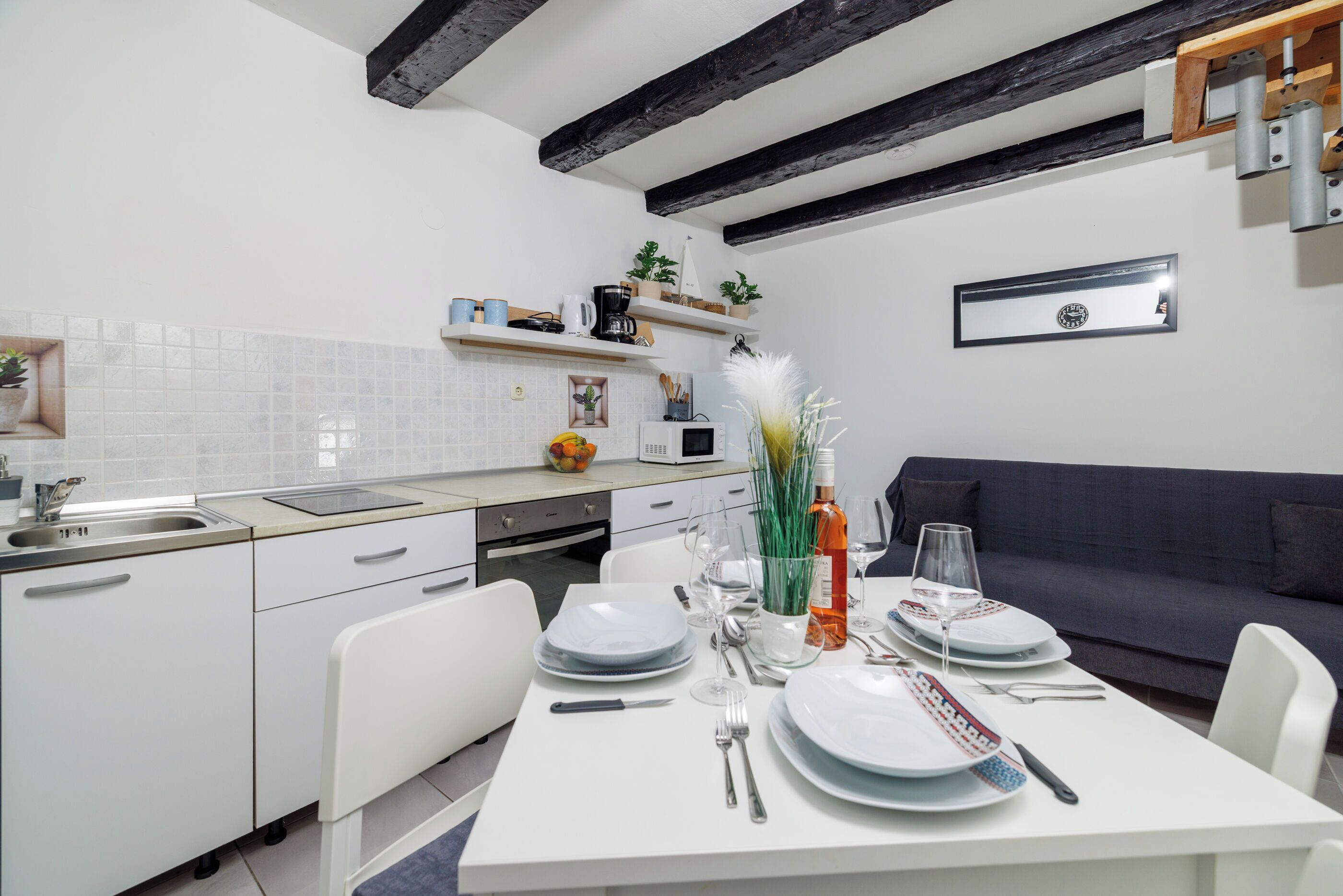 A modern kitchen with white cabinets, a dining table set for four, and a dark blue sofa in the adjacent living area.