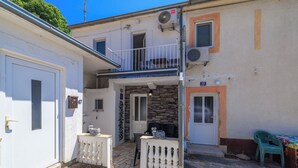 A small, two-story building with a balcony, a door with a number plate, and a small outdoor seating area with a table and chairs. - Apartment Lozann (Povile)