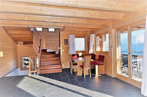 A wooden cabin interior with a staircase, a dining area, and a balcony with a view. - Aarninkhof (Bettmeralp)