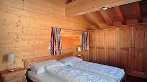 Quarto de cabana de madeira com uma cama de casal, guarda-roupa de madeira e cortinas.
