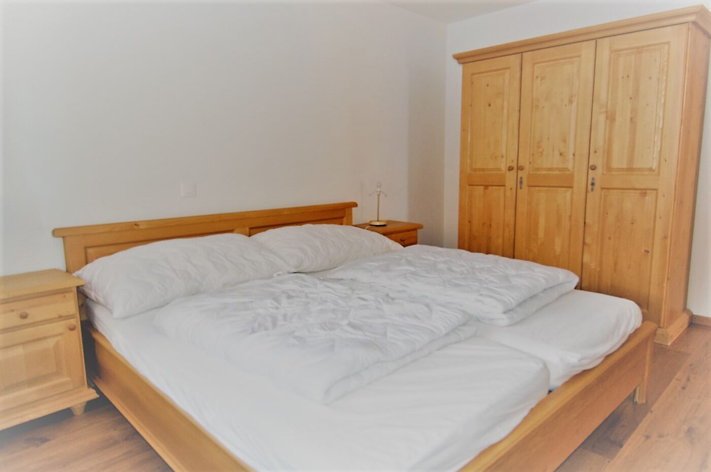 A bedroom with a wooden bed, a nightstand, and a wooden wardrobe.