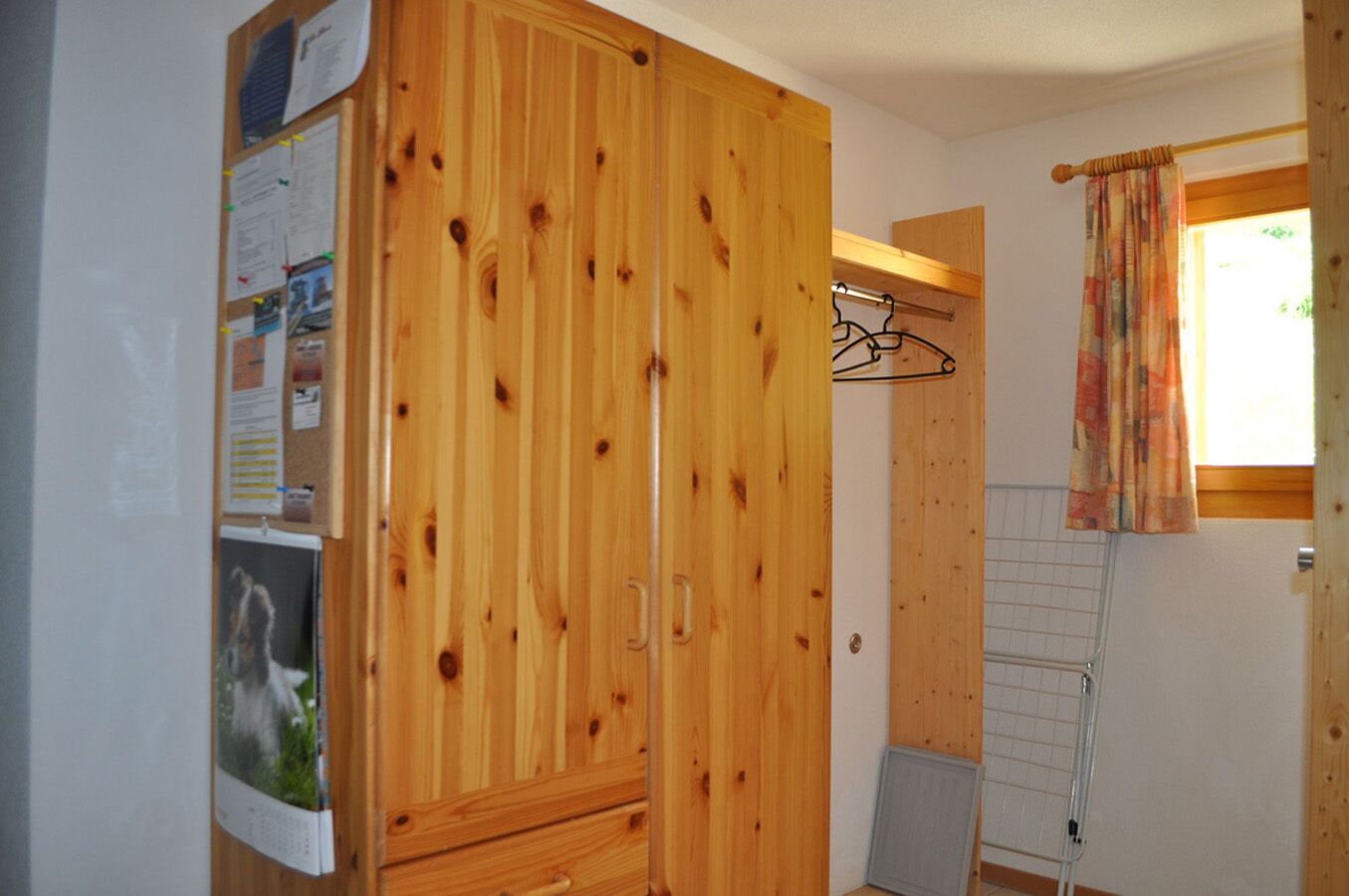 A wooden wardrobe with a mirror, a drying rack, and a window with curtains.