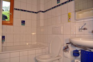 Un baño con azulejos blancos, una bañera, un inodoro y un lavamanos.