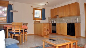 Una cocina compacta con armarios de madera, un comedor con mesa y sillas, y un ventanal con cortinas.