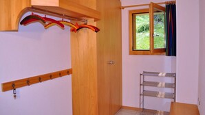 Una habitación con puerta de madera, un perchero con ganchos, una ventana con cortinas y una estantería metálica.