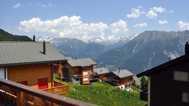 Un pueblo de montaña con casas de madera, una terraza de madera y vistas a montañas nevadas.