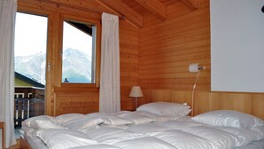 Un dormitorio de cabaña de madera con una cama grande, una ventana con cortinas y vistas a montañas.