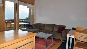 Una sala de estar acogedora con una mesa de madera, un sofá y vistas a las montañas a través de amplios ventanales.