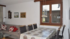 Una sala de estar con un sofá, una mesa de comedor con sillas, un ventanal con cortinas, un reloj de pared y dos cuadros enmarcados.