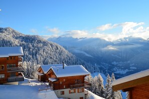 A wooden cabin with a balcony, surrounded by snow-covered trees and mountains. - Alpenglück 43 (Bettmeralp)