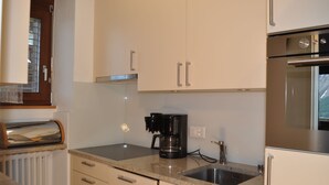 Una cocina con armarios blancos, una cafetera negra, un lavabo de acero inoxidable y una ventana con vistas.
