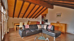 A living room with a sectional sofa, a glass coffee table, wooden flooring, and exposed wooden beams on the ceiling. - Alpenglück 51 (Bettmeralp)