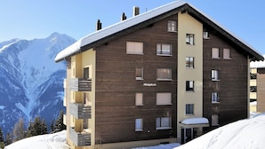 A multi-story building with a wooden facade, balconies, and a snow-covered roof. - Alpenglück 51 (Bettmeralp)