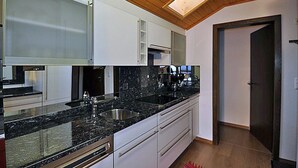 A modern kitchen with a granite countertop, stainless steel sink, and white cabinetry. - Alpenglück 51 (Bettmeralp)