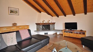 A living room with a fireplace, a sofa, a television, and wooden cabinets. - Alpenglück 51 (Bettmeralp)