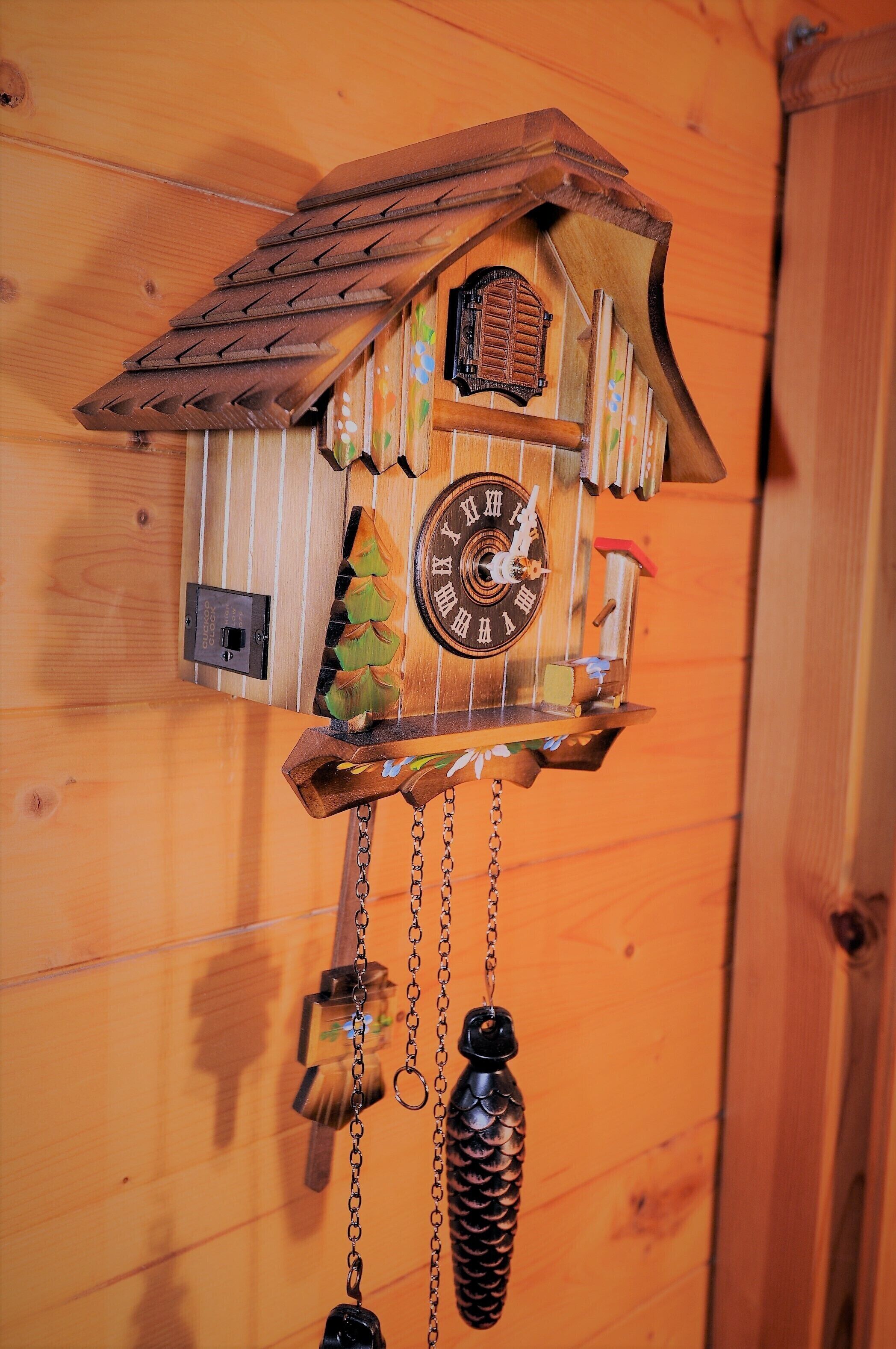 A cuckoo clock with a house design, featuring a clock face, a bird figure, and a pine cone decoration.
