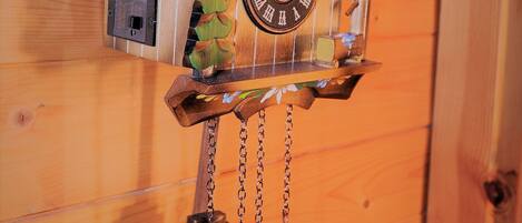 A cuckoo clock with a house design, featuring a clock face, a bird figure, and a pine cone decoration.