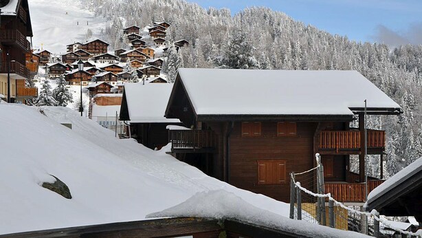 Un villaggio montano imbiancato dalla neve con edifici in legno, tra cui una lodge ben visibile con un balcone.