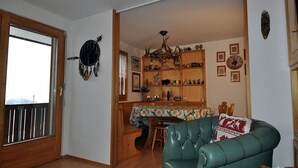 Zona pranzo con tavolo in legno, sedie e un lampadario. C'è un divano in pelle verde e una libreria in legno con diversi oggetti.