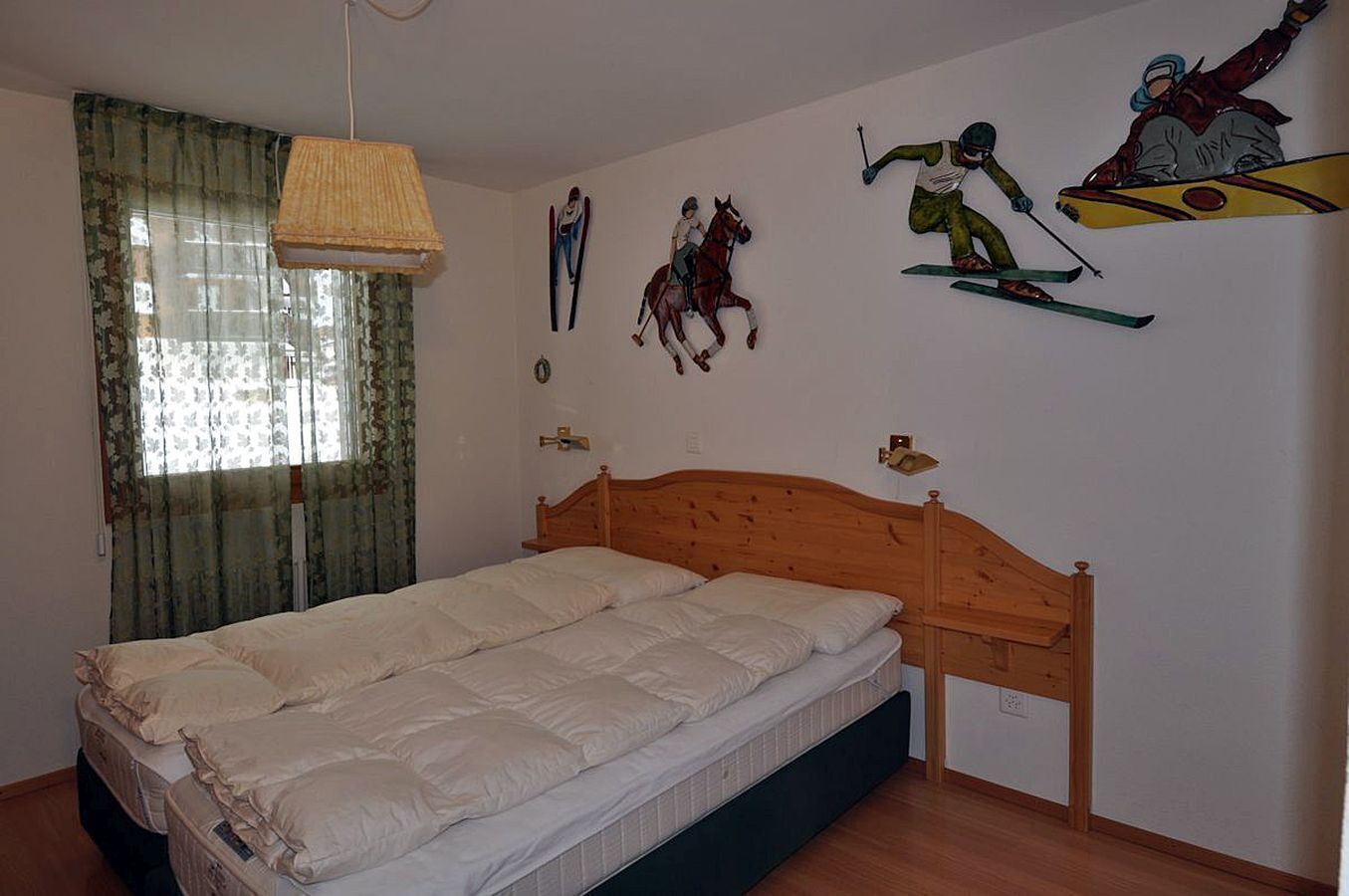 A bedroom with a wooden bed, a window with curtains, and wall art depicting skiing and horse riding.