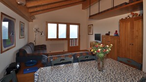 A cozy room with a wooden ceiling, a sofa, a dining table with a vase of flowers, and a window with a view. - Ambiente B21 (Bettmeralp)