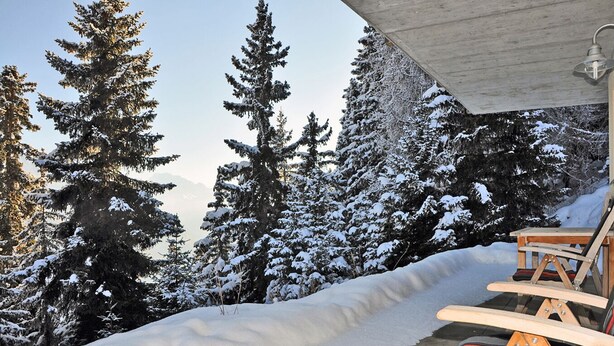 A wooden deck with a chair, surrounded by snow-covered trees and a clear sky. - Bettmerlodge (Bettmeralp)