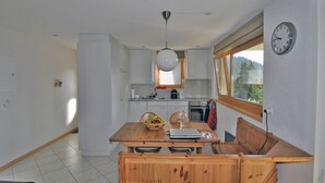 A compact kitchen with white cabinets, a wooden dining table, and a built-in bench. - Bettmerlodge (Bettmeralp)