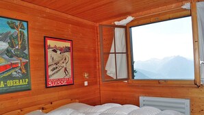 Habitació d'una cabana de fusta amb un llit, una finestra amb vista a les muntanyes i dos cartells a la paret.