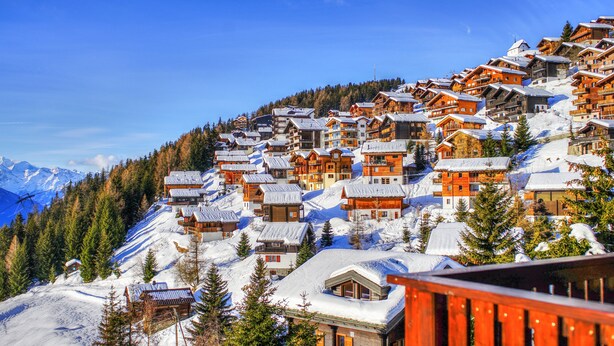 Un pueblo cubierto de nieve en la montaña, con casas de madera y un telesilla.