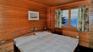 Habitación de cabaña de madera con cama, mesita de noche, un cuadro en la pared y ventana con cortinas.