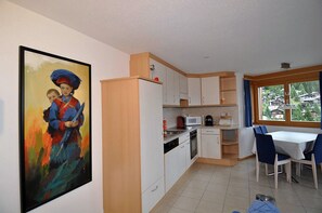 Kompakti keittiö, jossa on nykyaikaiset kodinkoneet, ruokailutila pöydän ja tuolien kera sekä suuri ikkuna, josta avautuu näkymä asuinalueelle.