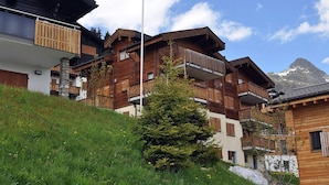 A multi-story wooden building with balconies, set against a mountainous backdrop. - Camelot 4 (Bettmeralp)