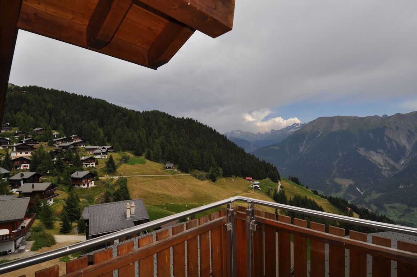 A wooden balcony overlooking a mountainous village with houses and a view of distant mountains.