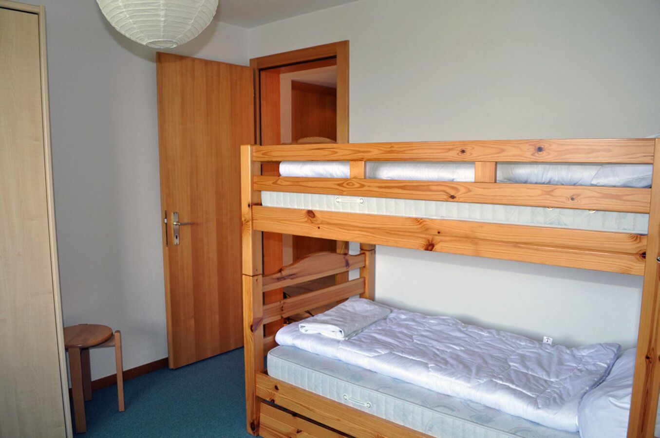 A bunk bed with a wooden frame, a small wooden chair, and a door in a room with light blue walls.