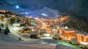 Un pueblo cubierto de nieve con edificios de madera, una pista de esquí y una montaña al fondo.