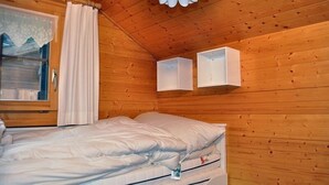 Habitación de cabaña de madera con una cama, una ventana con cortinas y dos armarios blancos en la pared.